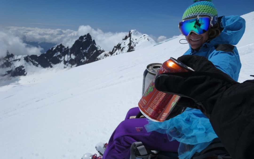 A woman in a ski hat, goggles, purple ski pants, and a tutu raises her beer in cheers to an unseen person with just a beer in hand off camera. They are enjoying a beer because the author does not drink coffee.