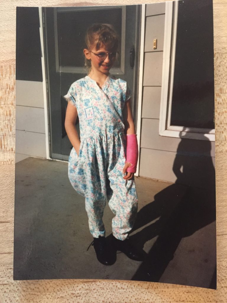 Young Kristina with pink glasses and a pink cast... in a romper?
