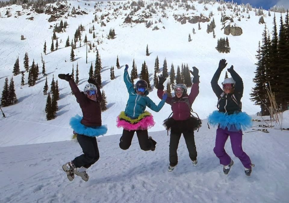 Four women in ski gear and tutus jump for joy.
