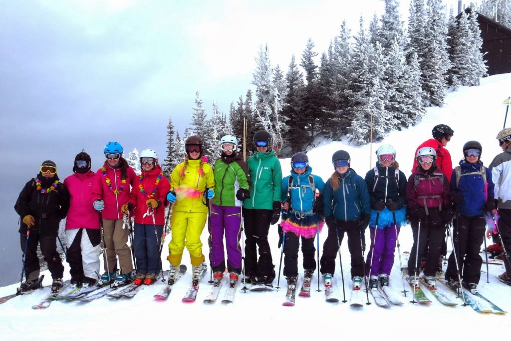 Women in ski gear line up in the order of a rainbow based on their outerwear colors.
