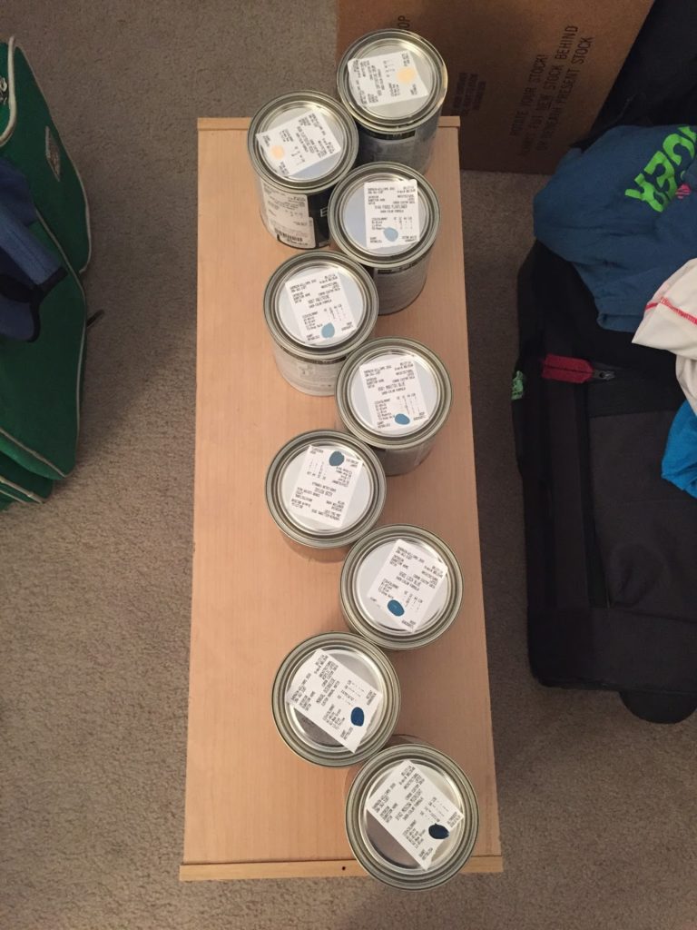 Nine small paint cans sit in a line, as seen from above.