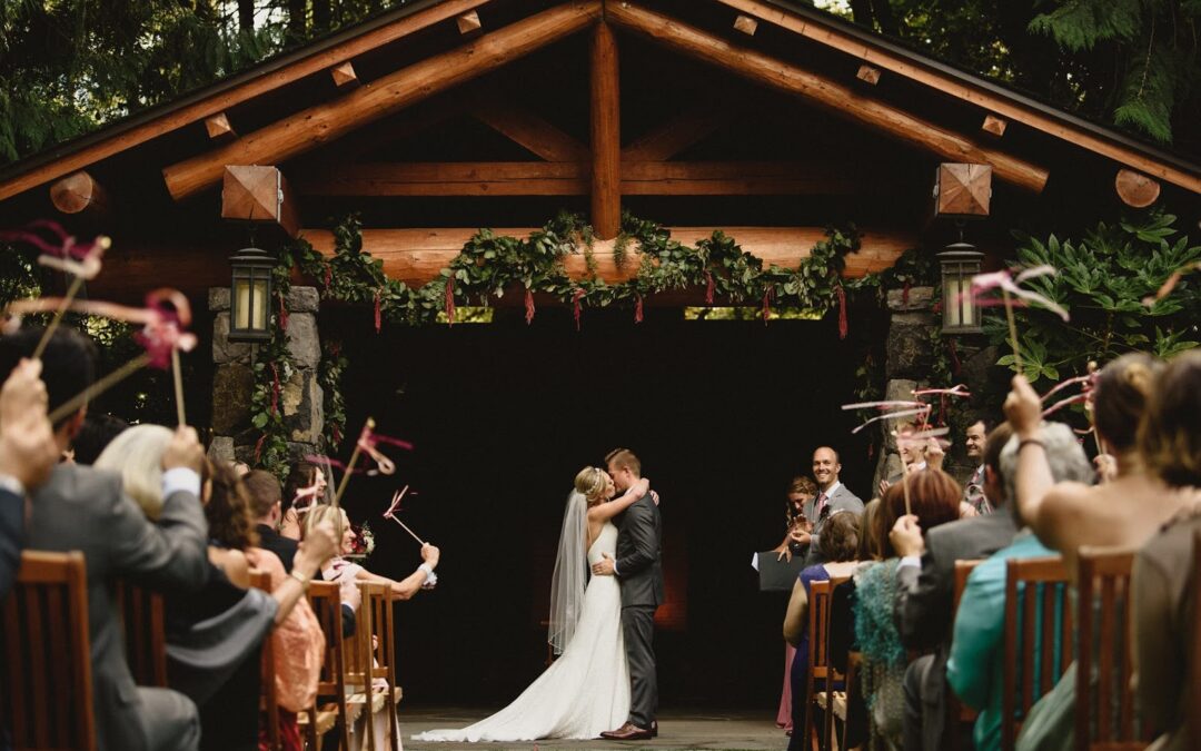 A picture of a bride and groom kissing at the alter, taken from the back of the aisle with the guests raising streamers in celebration.