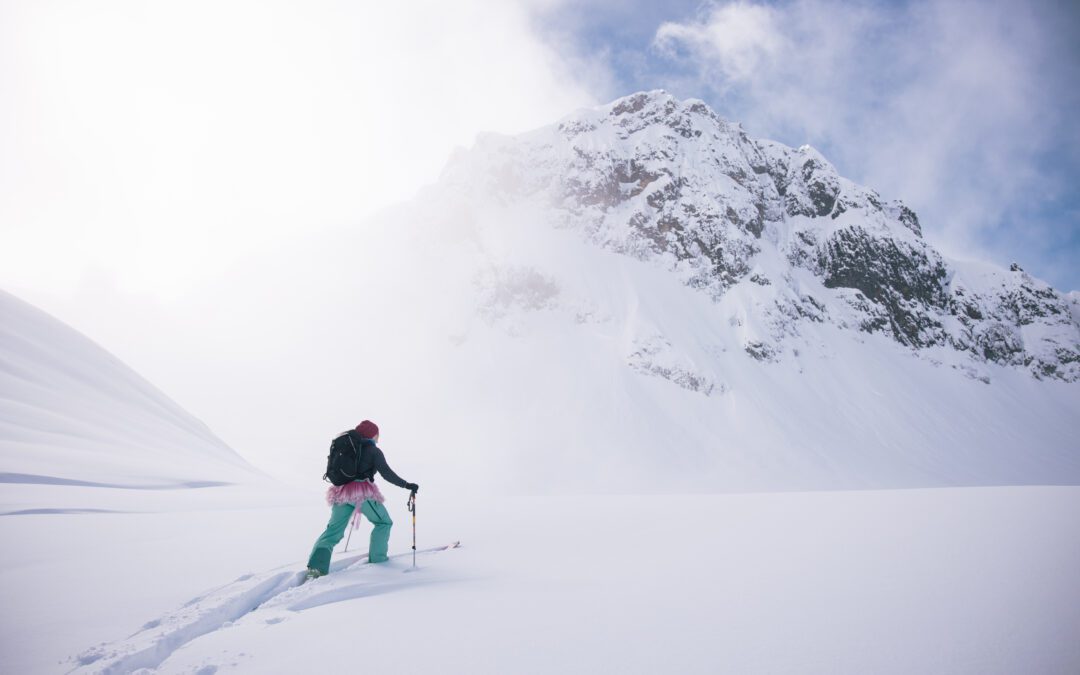 A backcountry skier in a pin tutu climbs into the clouds surrounded by snow.