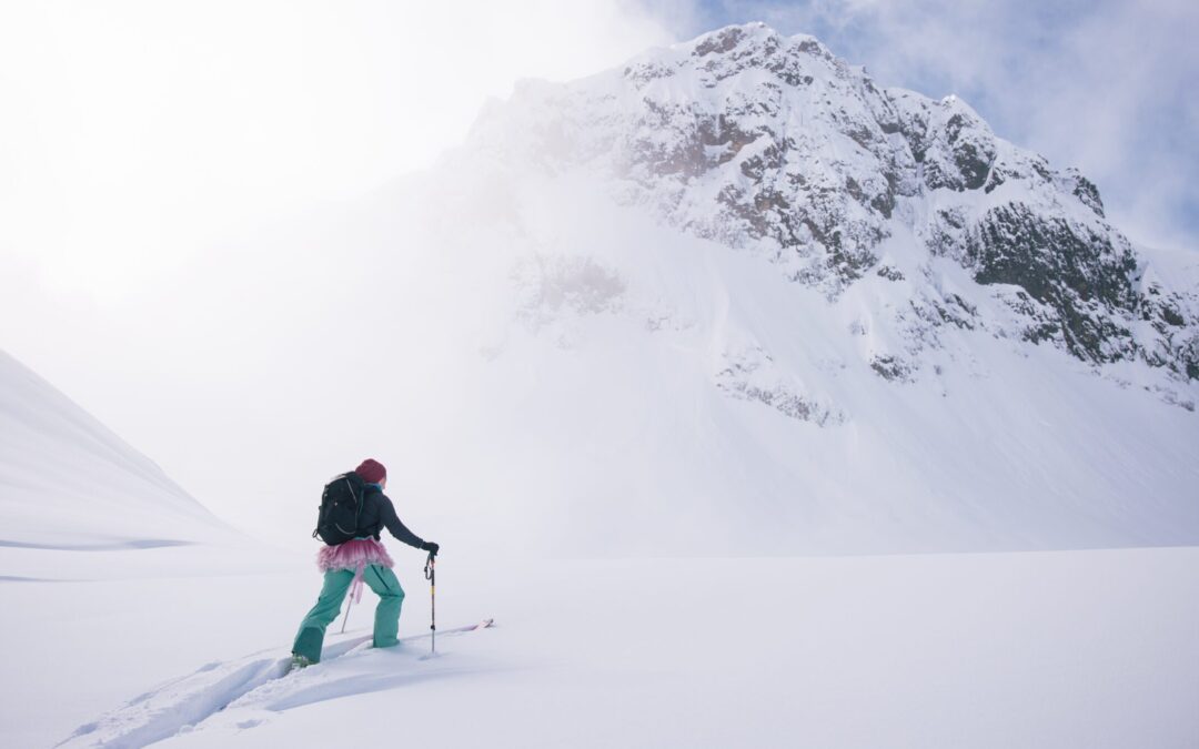 A backcountry skier in a pin tutu climbs into the clouds surrounded by snow.