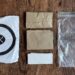 A photo of a deconstructed poop kit, including a sealing plastic bag, two paper bags, toilet paper, and target.